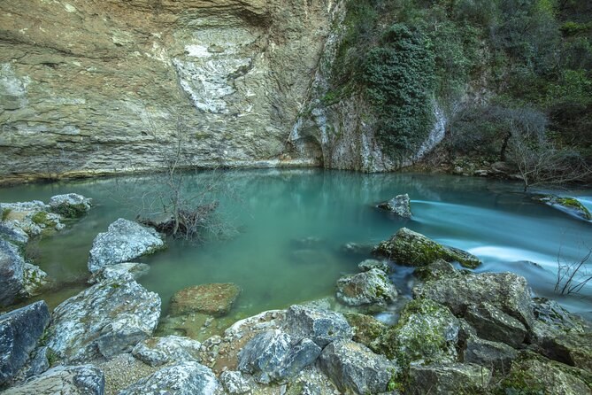 A clear green pool of spring water at the foot of a grey cliff